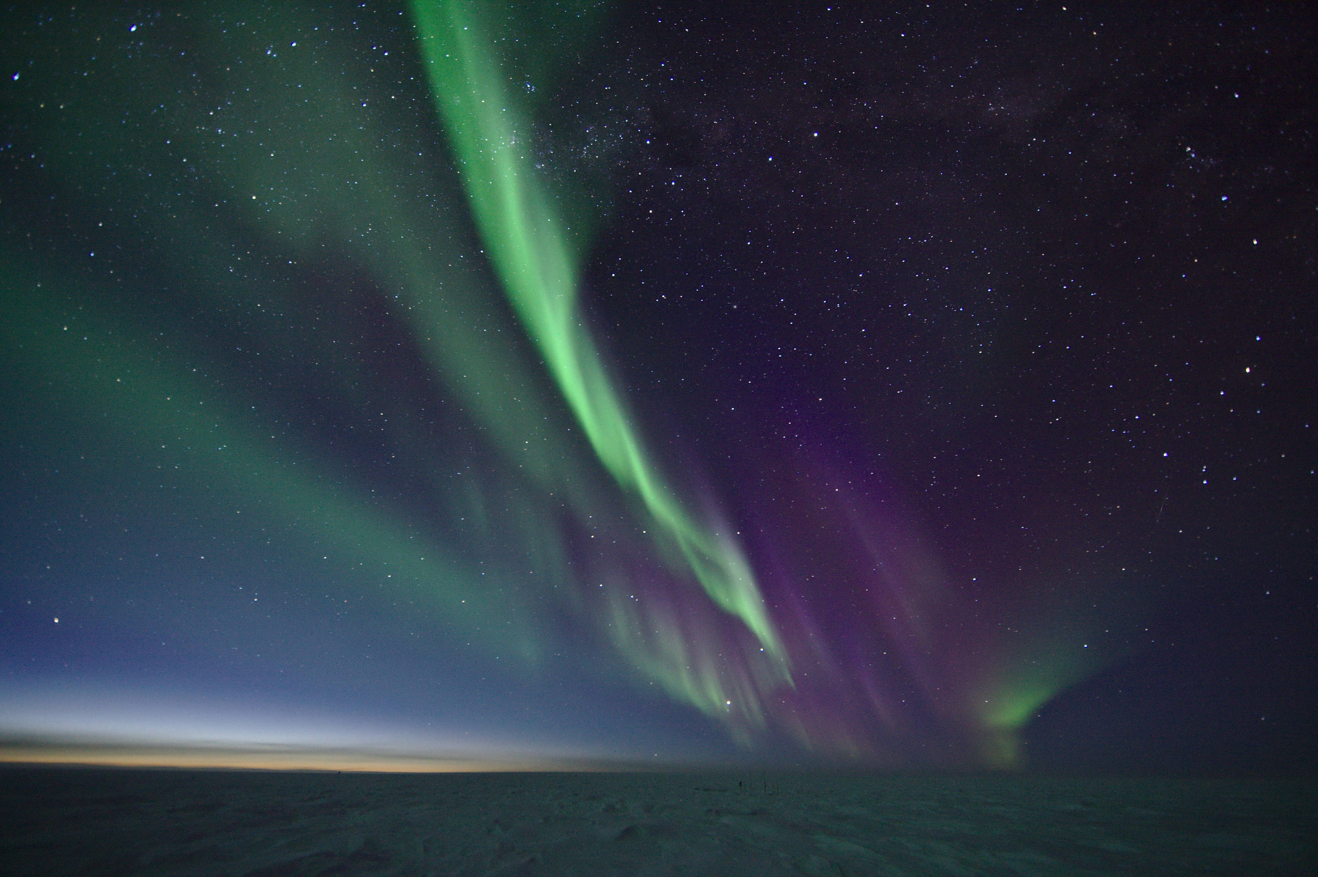 View outside - the frozen landscape of the south pole illuminated by beautiful auroras and a tiny glimpse of sunlight